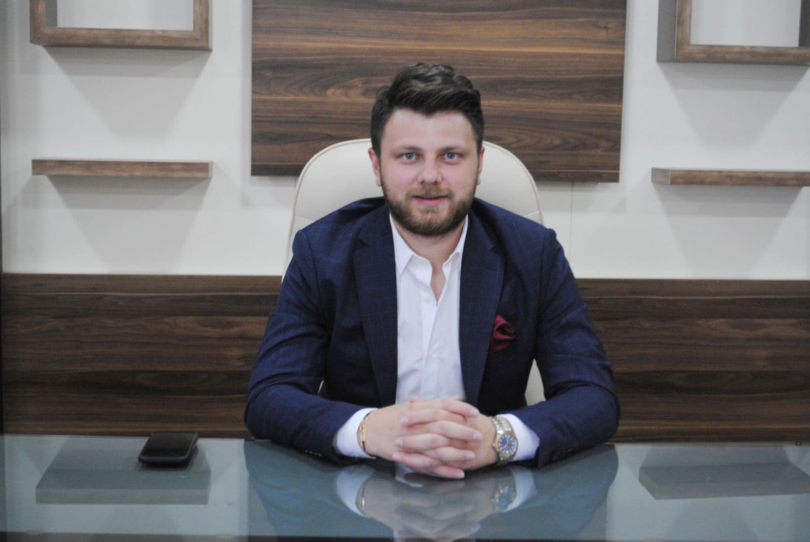 Ömer Yazıcıoğlu at a glass desk in a wood-panelled office