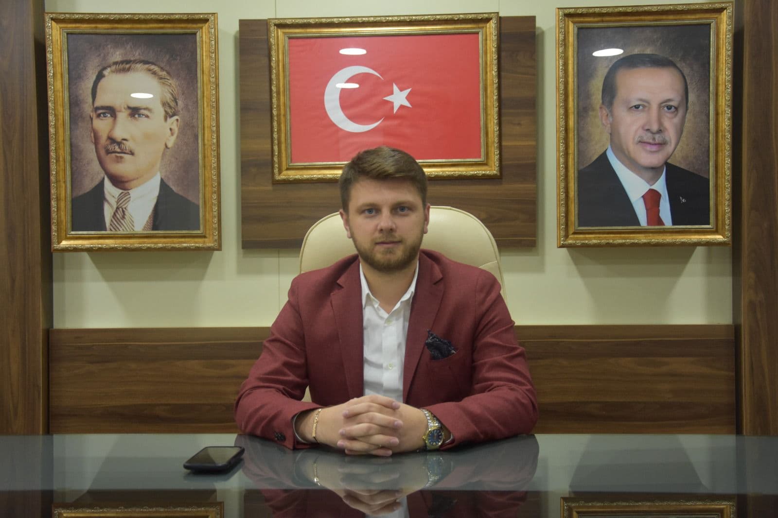 Ömer Yazıcıoğlu at his desk in an office hung with a Turkish flag and portraits of Atatürk and the President