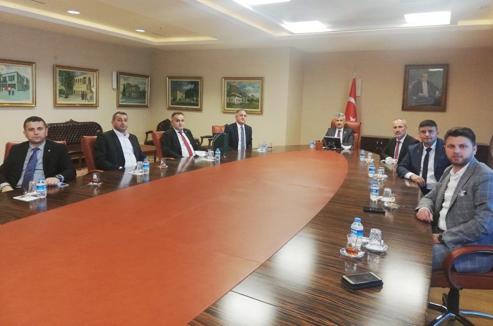 A formal meeting of eight people around a long conference table