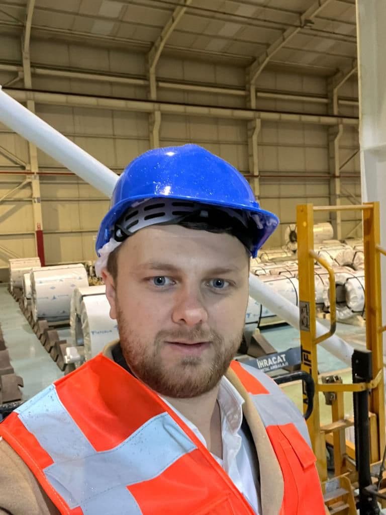 Ömer Yazıcıoğlu in a hard hat on a factory floor stacked with steel coils