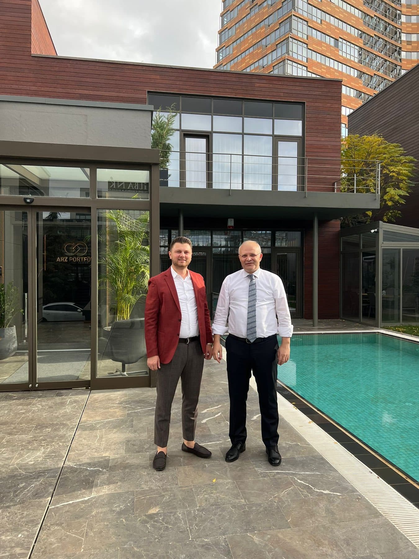 Ömer Yazıcıoğlu with another person at the entrance of a business centre with a pool